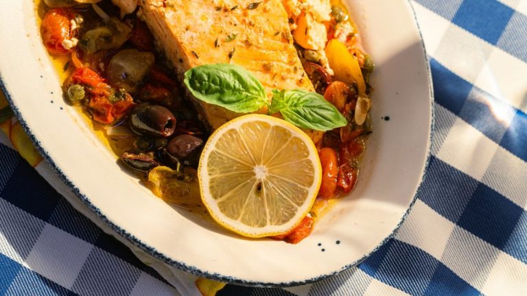 Delicious grilled salmon topped with lemon and basil on a sunlit table.